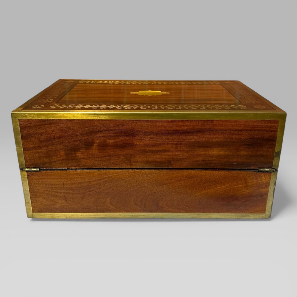 A rectangular dark timber writing slope featuring brass edge binding, intricate brass foliate inlay, a central brass nameplate, and a brass keyhole escutcheon. View VIII