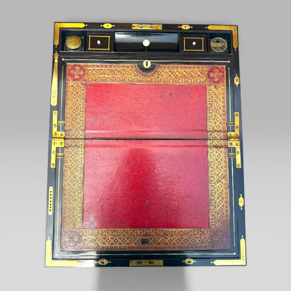 A rectangular dark timber writing slope featuring brass edge binding, intricate brass foliate inlay, a central brass nameplate, and a brass keyhole escutcheon. View IX