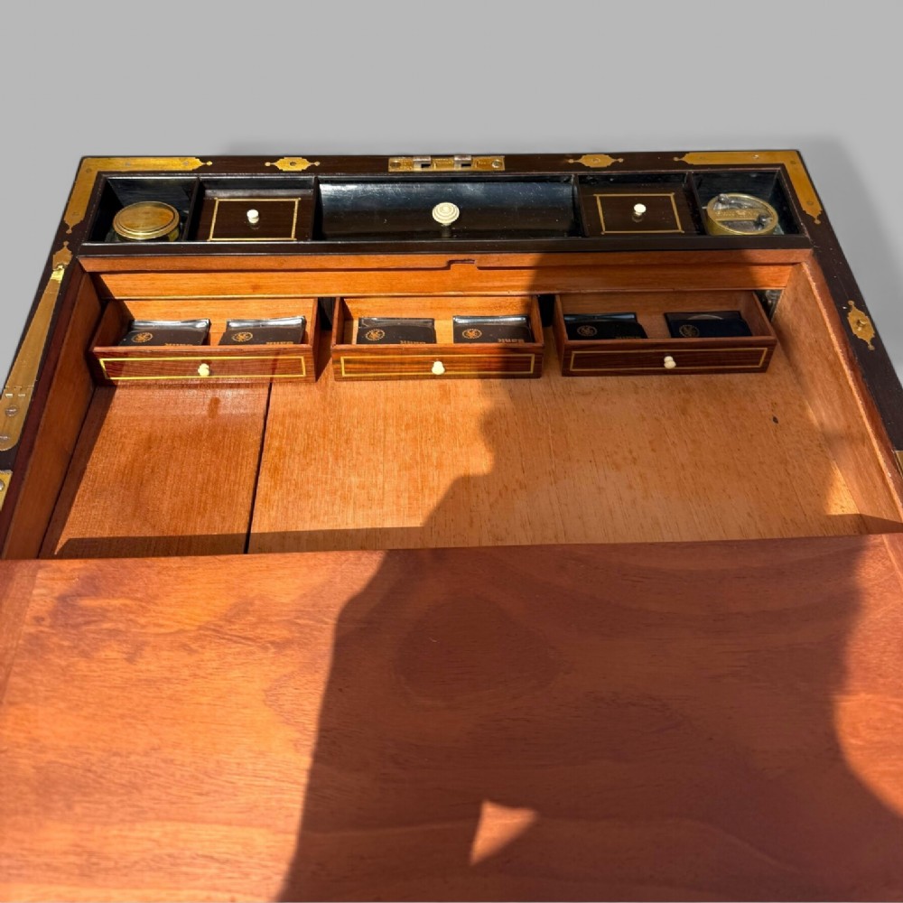 A rectangular dark timber writing slope featuring brass edge binding, intricate brass foliate inlay, a central brass nameplate, and a brass keyhole escutcheon. View XII