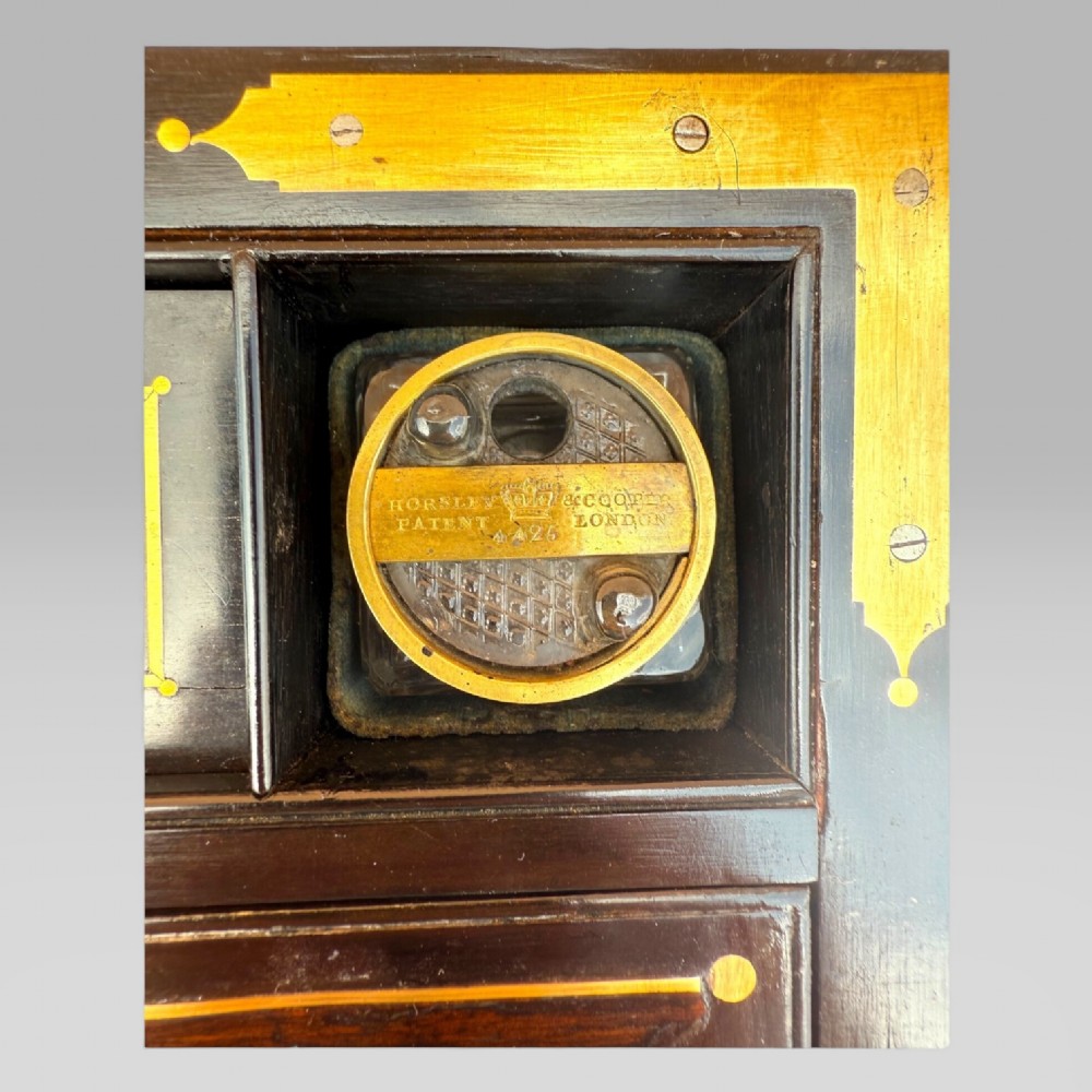 A rectangular dark timber writing slope featuring brass edge binding, intricate brass foliate inlay, a central brass nameplate, and a brass keyhole escutcheon. View XIV