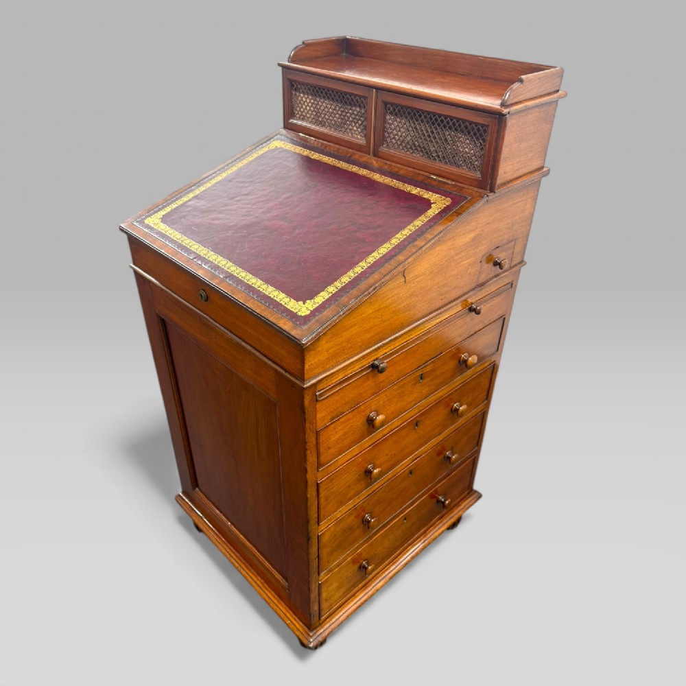 An antique mahogany Davenport desk featuring a sloped red leather writing surface, turned drawer knobs, and a top gallery superstructure.