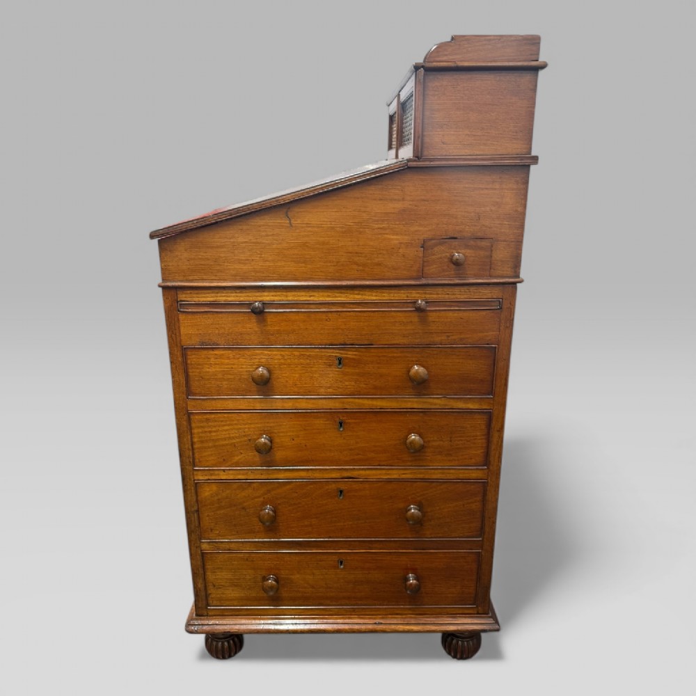 An antique mahogany Davenport desk featuring a sloped red leather writing surface, turned drawer knobs, and a top gallery superstructure. View III