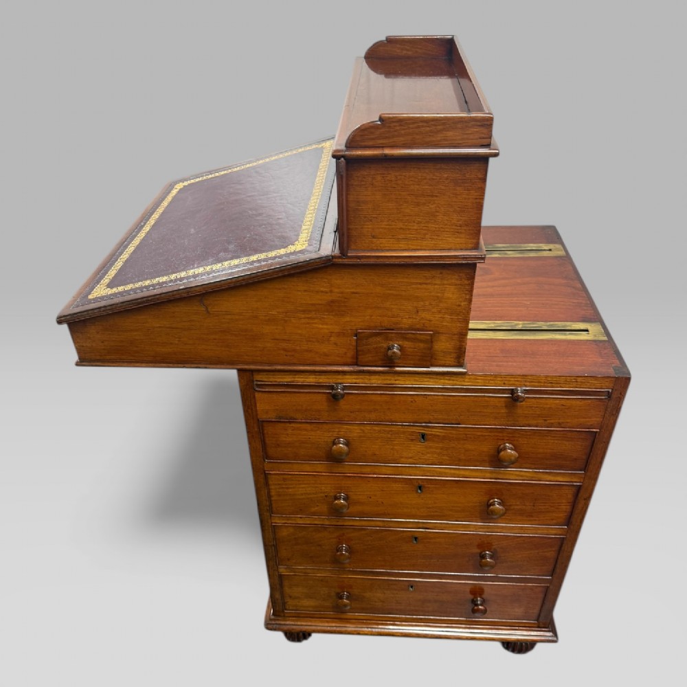 An antique mahogany Davenport desk featuring a sloped red leather writing surface, turned drawer knobs, and a top gallery superstructure. View X