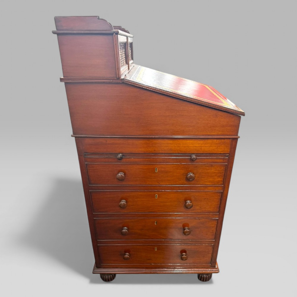 An antique mahogany Davenport desk featuring a sloped red leather writing surface, turned drawer knobs, and a top gallery superstructure. View XIV