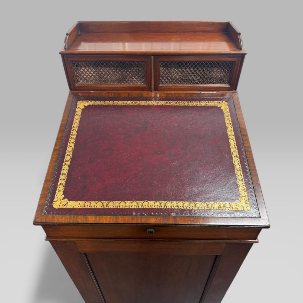 An antique mahogany Davenport desk featuring a sloped red leather writing surface, turned drawer knobs, and a top gallery superstructure. View XV
