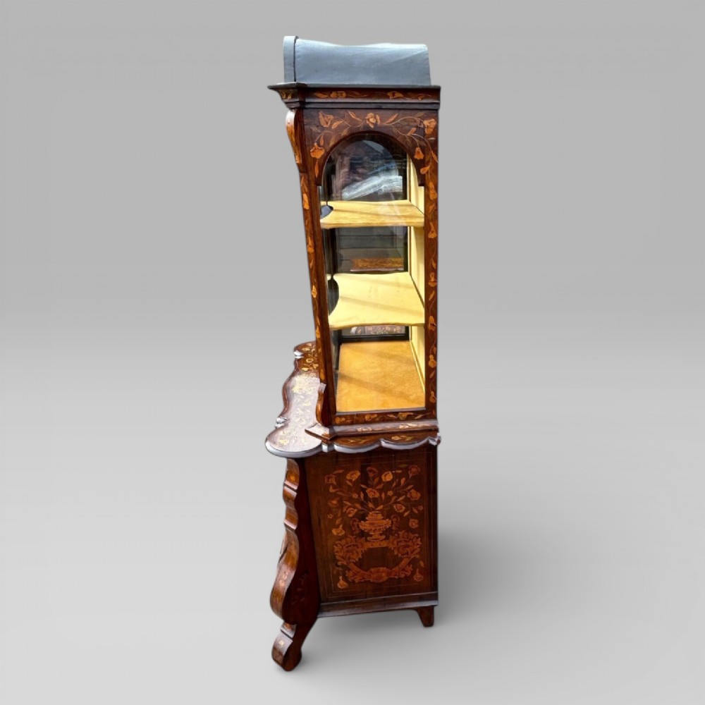 An antique walnut display cabinet on a bombe chest of drawers featuring floral marquetry inlay, glazed doors, and brass handles. View V