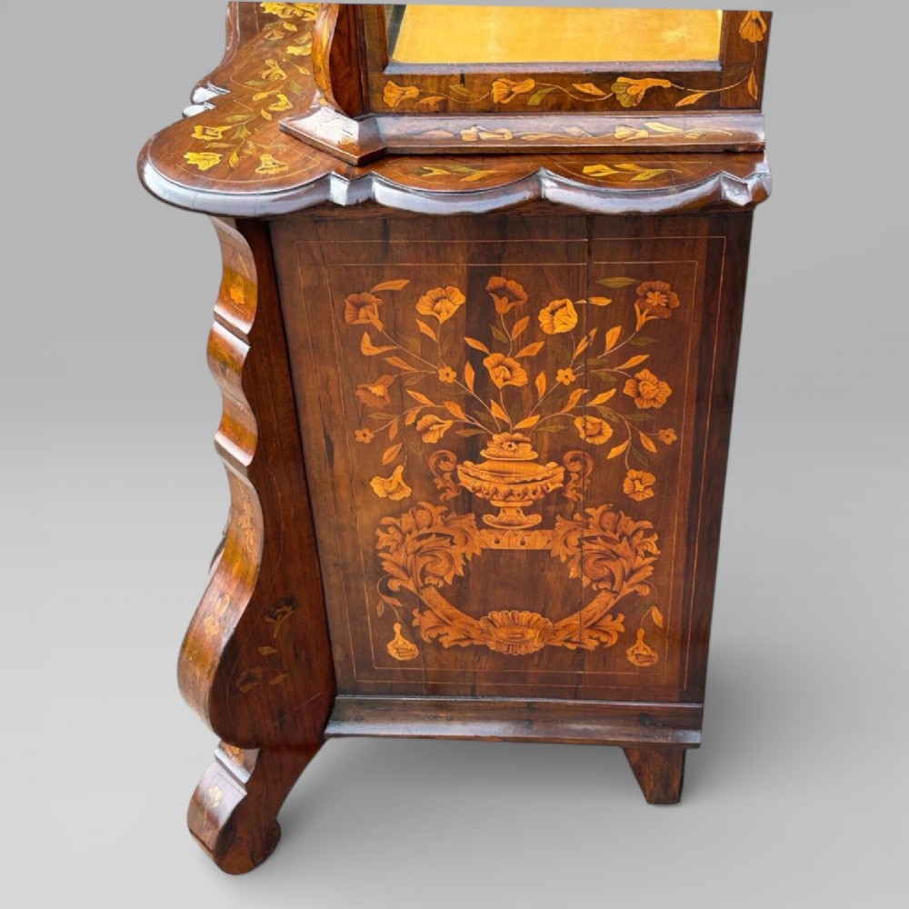 An antique walnut display cabinet on a bombe chest of drawers featuring floral marquetry inlay, glazed doors, and brass handles. View VI