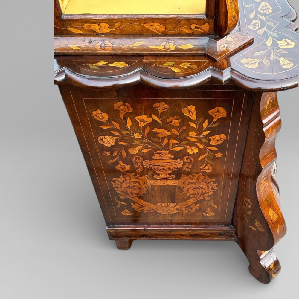 An antique walnut display cabinet on a bombe chest of drawers featuring floral marquetry inlay, glazed doors, and brass handles. View VII