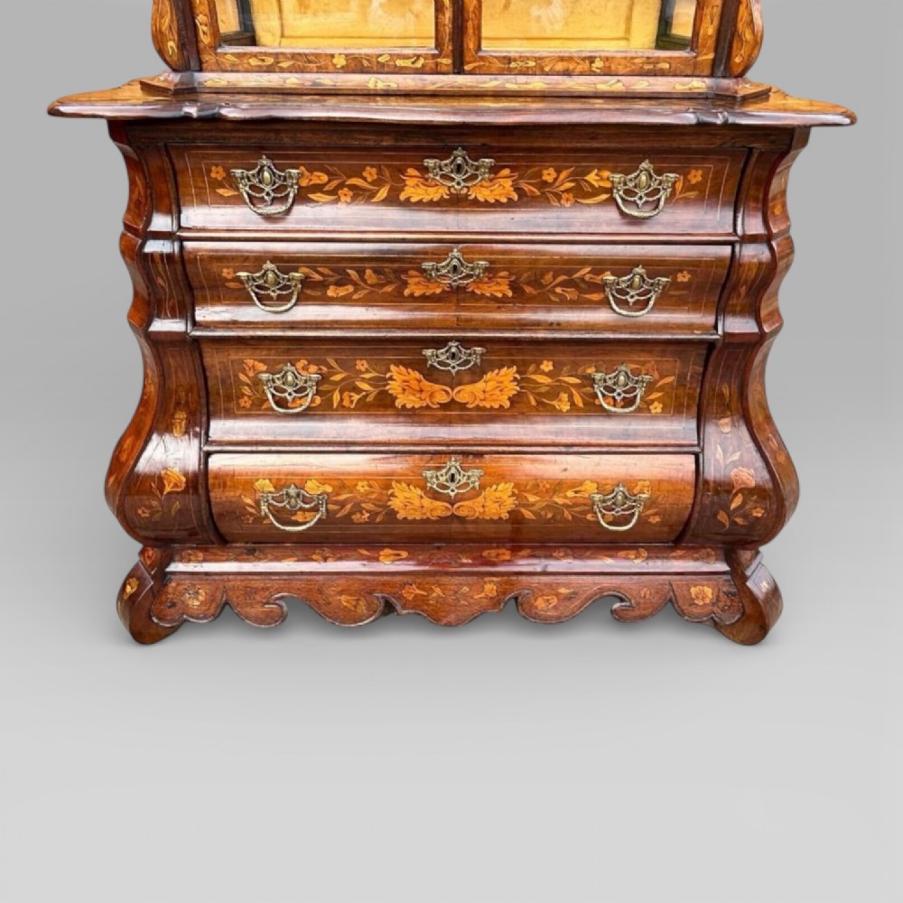 An antique walnut display cabinet on a bombe chest of drawers featuring floral marquetry inlay, glazed doors, and brass handles. View XII