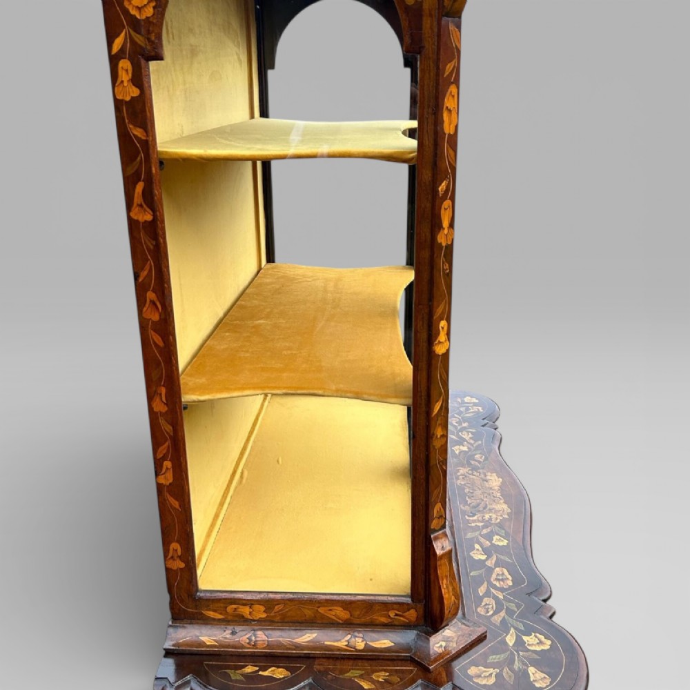 An antique walnut display cabinet on a bombe chest of drawers featuring floral marquetry inlay, glazed doors, and brass handles. View XV