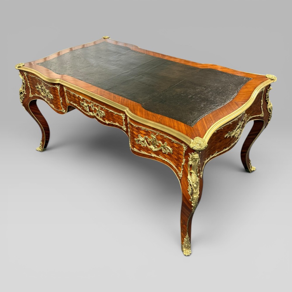 A Louis XV style kingwood parquetry bureau plat featuring a dark leather writing surface, cabriole legs, and gilt-bronze ormolu mounts. View IV