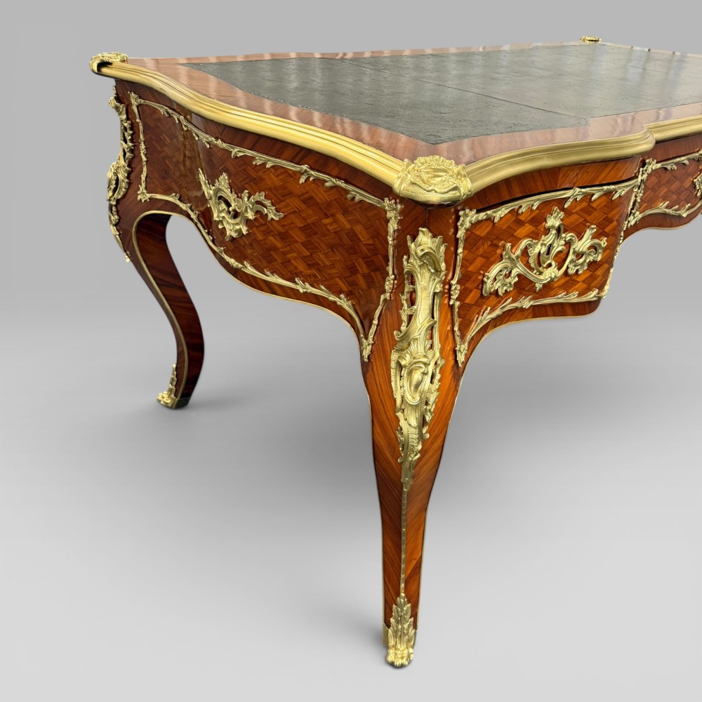 A Louis XV style kingwood parquetry bureau plat featuring a dark leather writing surface, cabriole legs, and gilt-bronze ormolu mounts. View V