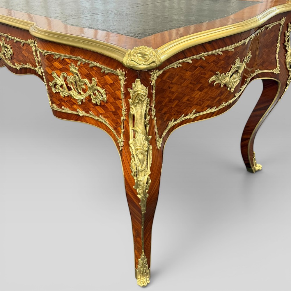 A Louis XV style kingwood parquetry bureau plat featuring a dark leather writing surface, cabriole legs, and gilt-bronze ormolu mounts. View VI