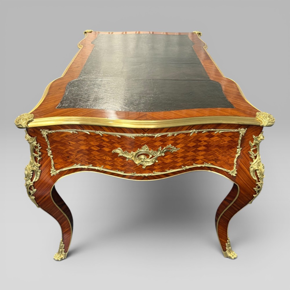 A Louis XV style kingwood parquetry bureau plat featuring a dark leather writing surface, cabriole legs, and gilt-bronze ormolu mounts. View VII