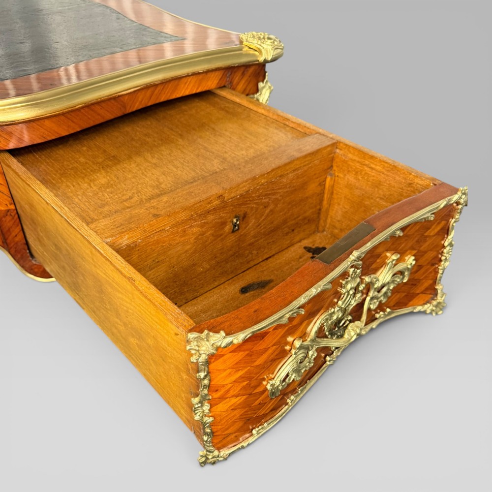 A Louis XV style kingwood parquetry bureau plat featuring a dark leather writing surface, cabriole legs, and gilt-bronze ormolu mounts. View X