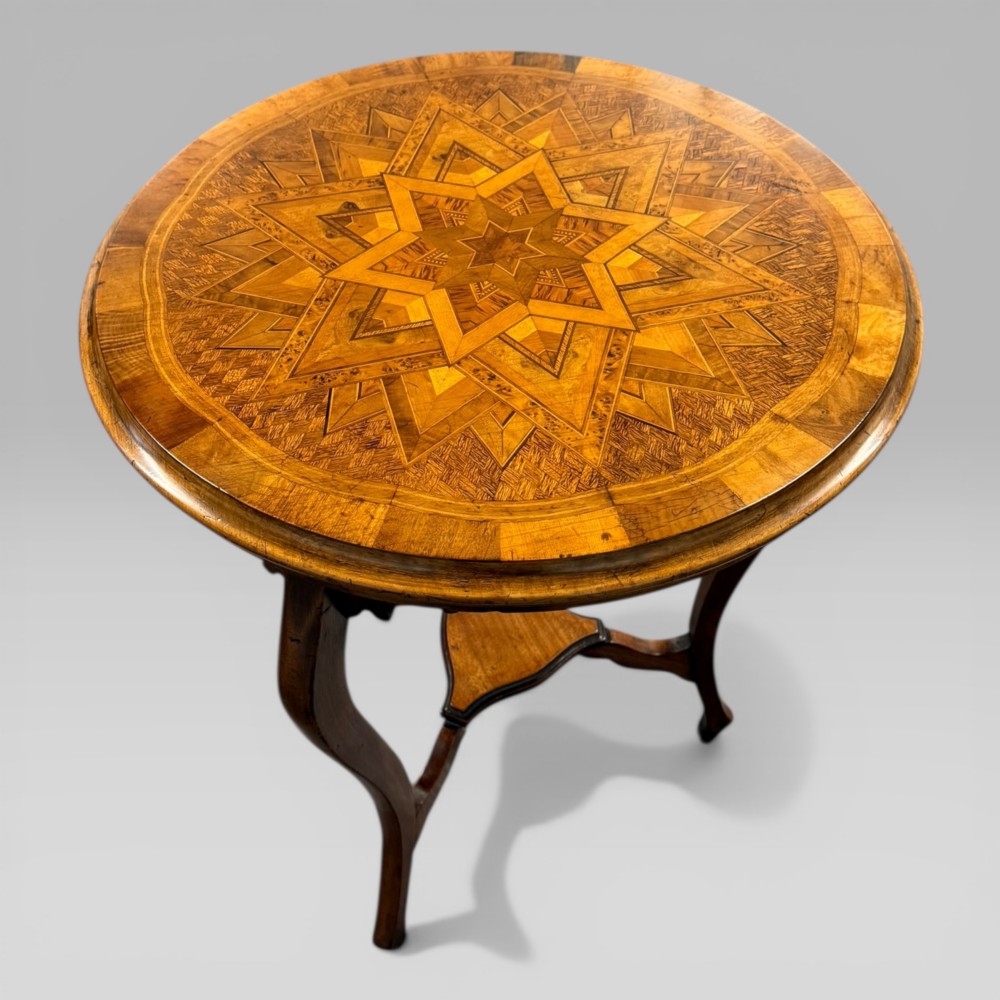 A circular antique side table featuring an intricate multi-timber geometric starburst marquetry pattern on top, set on carved cabriole legs with a triangular lower tier.