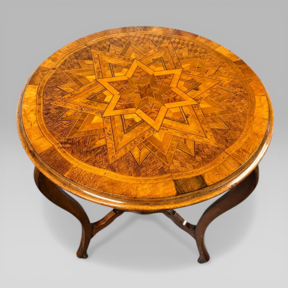 A circular antique side table featuring an intricate multi-timber geometric starburst marquetry pattern on top, set on carved cabriole legs with a triangular lower tier. View II