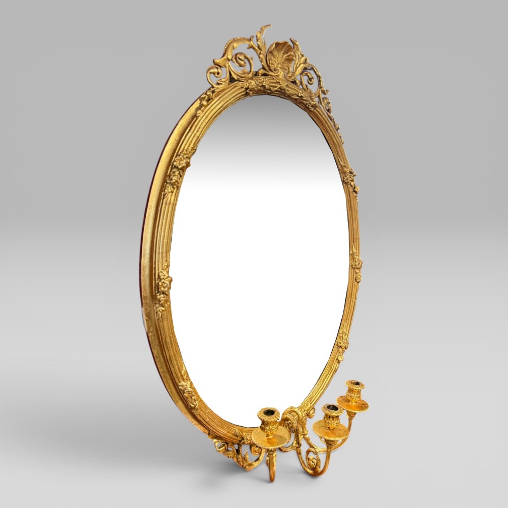 An oval giltwood mirror framed with floral carving and a top shell crest, featuring three candle sconces mounted at the base. View II