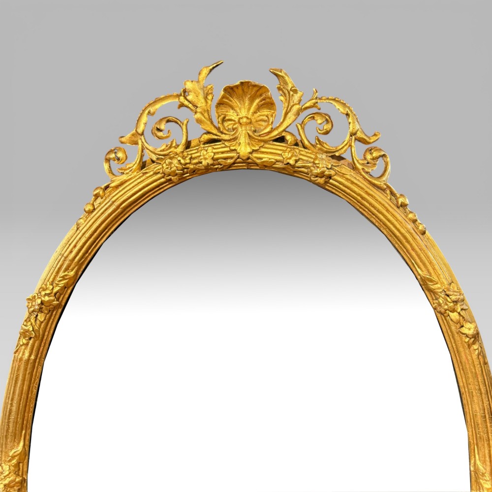 An oval giltwood mirror framed with floral carving and a top shell crest, featuring three candle sconces mounted at the base. View III