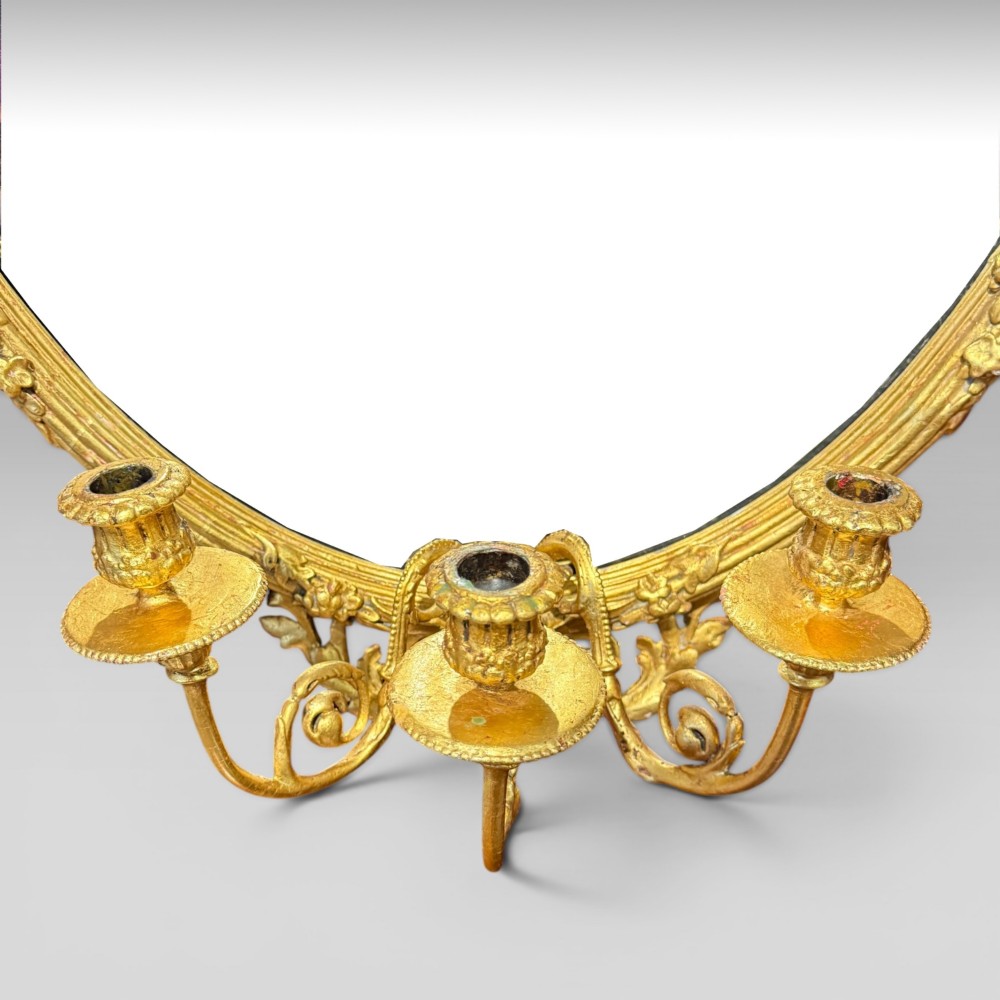 An oval giltwood mirror framed with floral carving and a top shell crest, featuring three candle sconces mounted at the base. View IV
