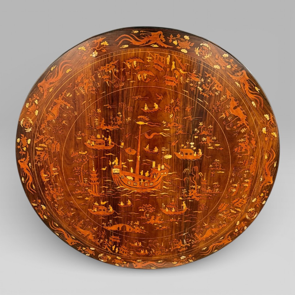 Circular rosewood centre table featuring detailed marquetry depictions of ships, pagodas, and floral motifs resting on a square inlaid pedestal base. View II