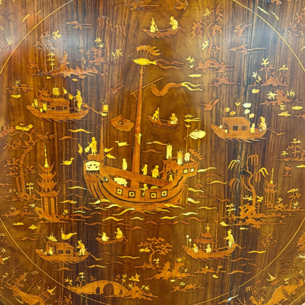 Circular rosewood centre table featuring detailed marquetry depictions of ships, pagodas, and floral motifs resting on a square inlaid pedestal base. View VII