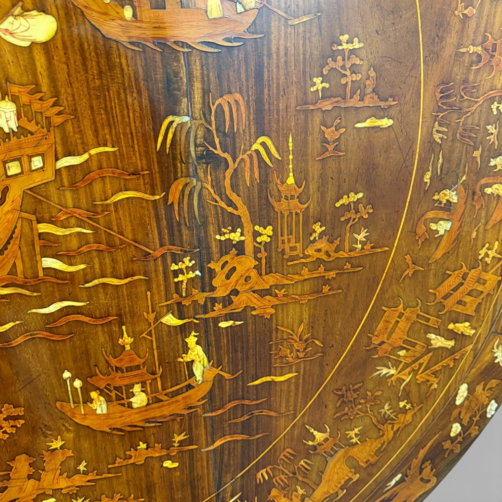 Circular rosewood centre table featuring detailed marquetry depictions of ships, pagodas, and floral motifs resting on a square inlaid pedestal base. View XII