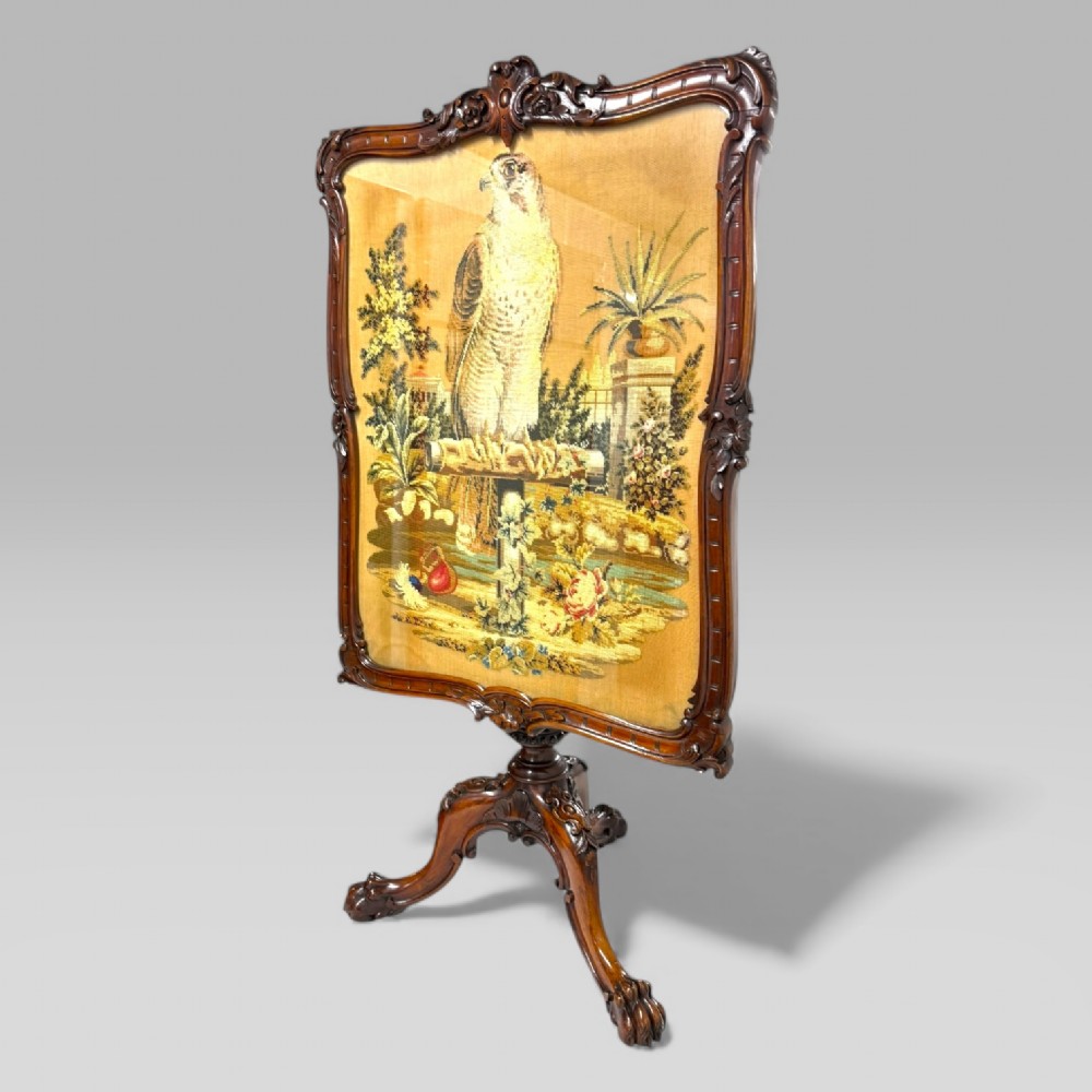 A William IV rosewood tilt-top tripod table featuring a shaped, carved frame housing a glazed needlepoint panel above a carved column and splayed tripod legs. View II