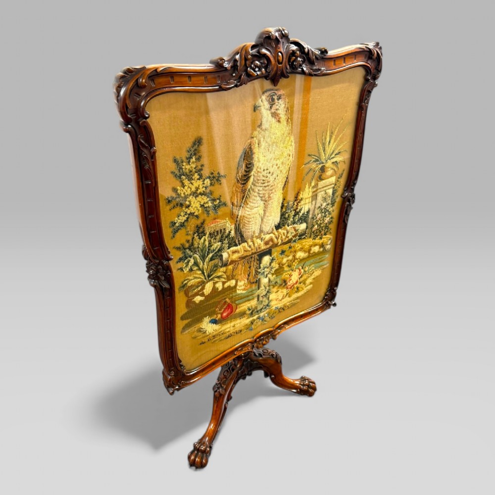 A William IV rosewood tilt-top tripod table featuring a shaped, carved frame housing a glazed needlepoint panel above a carved column and splayed tripod legs. View III