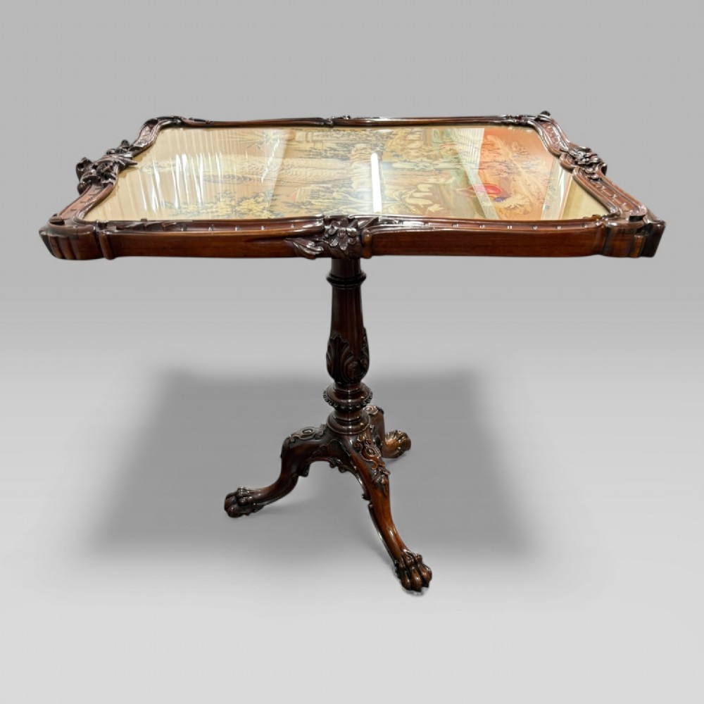 A William IV rosewood tilt-top tripod table featuring a shaped, carved frame housing a glazed needlepoint panel above a carved column and splayed tripod legs. View VII