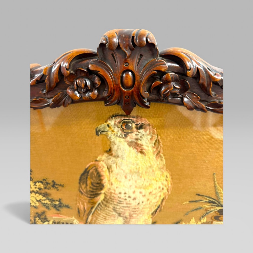 A William IV rosewood tilt-top tripod table featuring a shaped, carved frame housing a glazed needlepoint panel above a carved column and splayed tripod legs. View IX