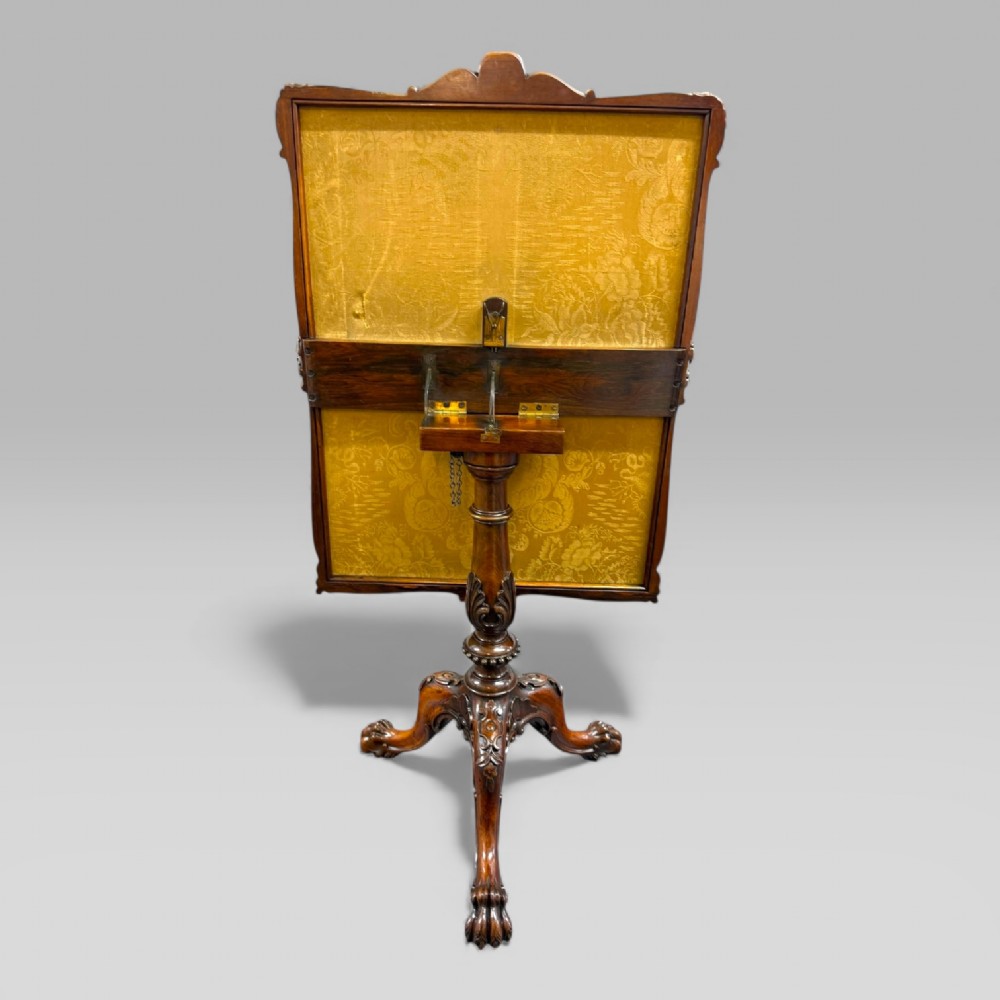 A William IV rosewood tilt-top tripod table featuring a shaped, carved frame housing a glazed needlepoint panel above a carved column and splayed tripod legs. View X