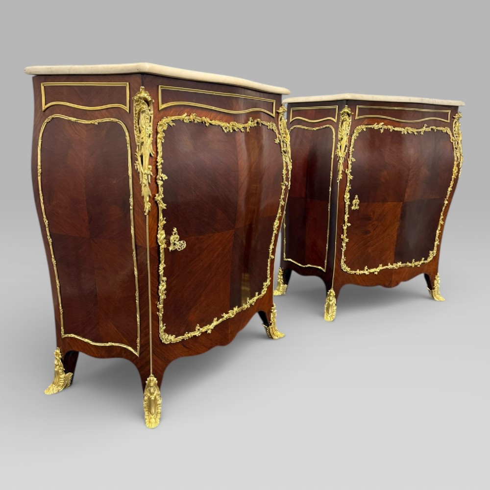 A pair of late 19th-century French kingwood bombe cabinets featuring ornate gilt-bronze mounts, curved fronts, and pale marble tops.
