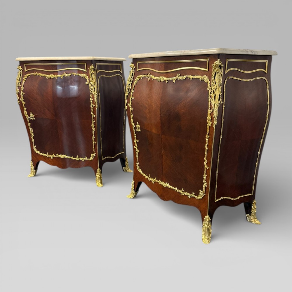 A pair of late 19th-century French kingwood bombe cabinets featuring ornate gilt-bronze mounts, curved fronts, and pale marble tops. View V