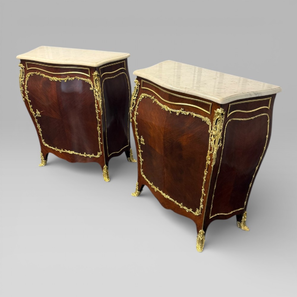 A pair of late 19th-century French kingwood bombe cabinets featuring ornate gilt-bronze mounts, curved fronts, and pale marble tops. View VI