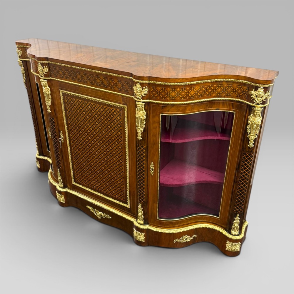 A Victorian walnut serpentine credenza featuring geometric marquetry, gilt ormolu mounts, a central panel door, and two curved glass side doors revealing lined display shelves. View III