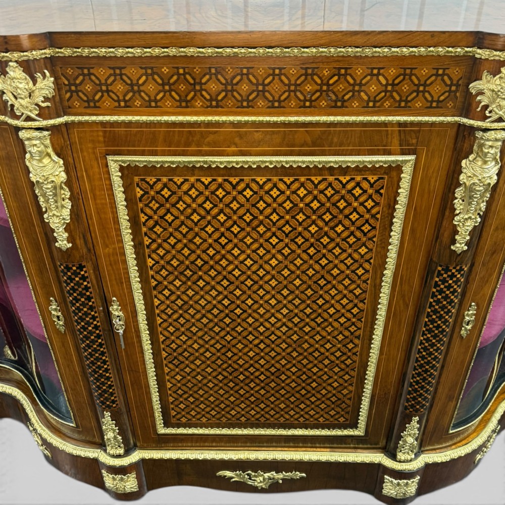 A Victorian walnut serpentine credenza featuring geometric marquetry, gilt ormolu mounts, a central panel door, and two curved glass side doors revealing lined display shelves. View V