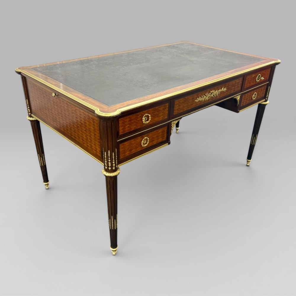A Louis XVI style mahogany and parquetry writing desk featuring a dark leather top, gilt-bronze mounts, five drawers, and fluted tapered legs. View II