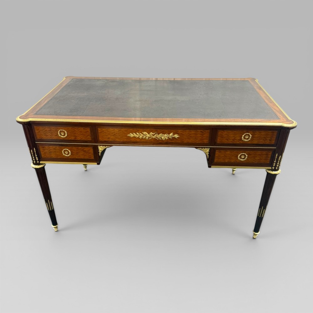 A Louis XVI style mahogany and parquetry writing desk featuring a dark leather top, gilt-bronze mounts, five drawers, and fluted tapered legs. View IV