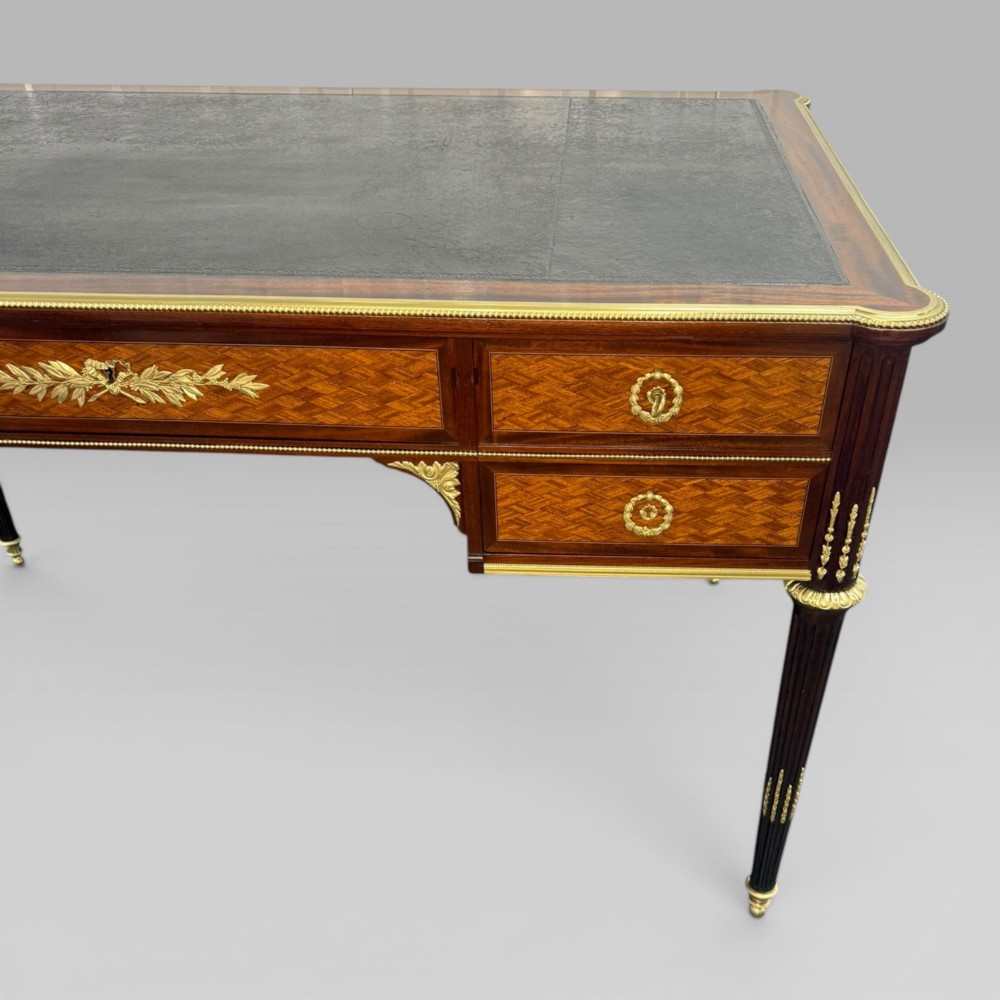 A Louis XVI style mahogany and parquetry writing desk featuring a dark leather top, gilt-bronze mounts, five drawers, and fluted tapered legs. View VII