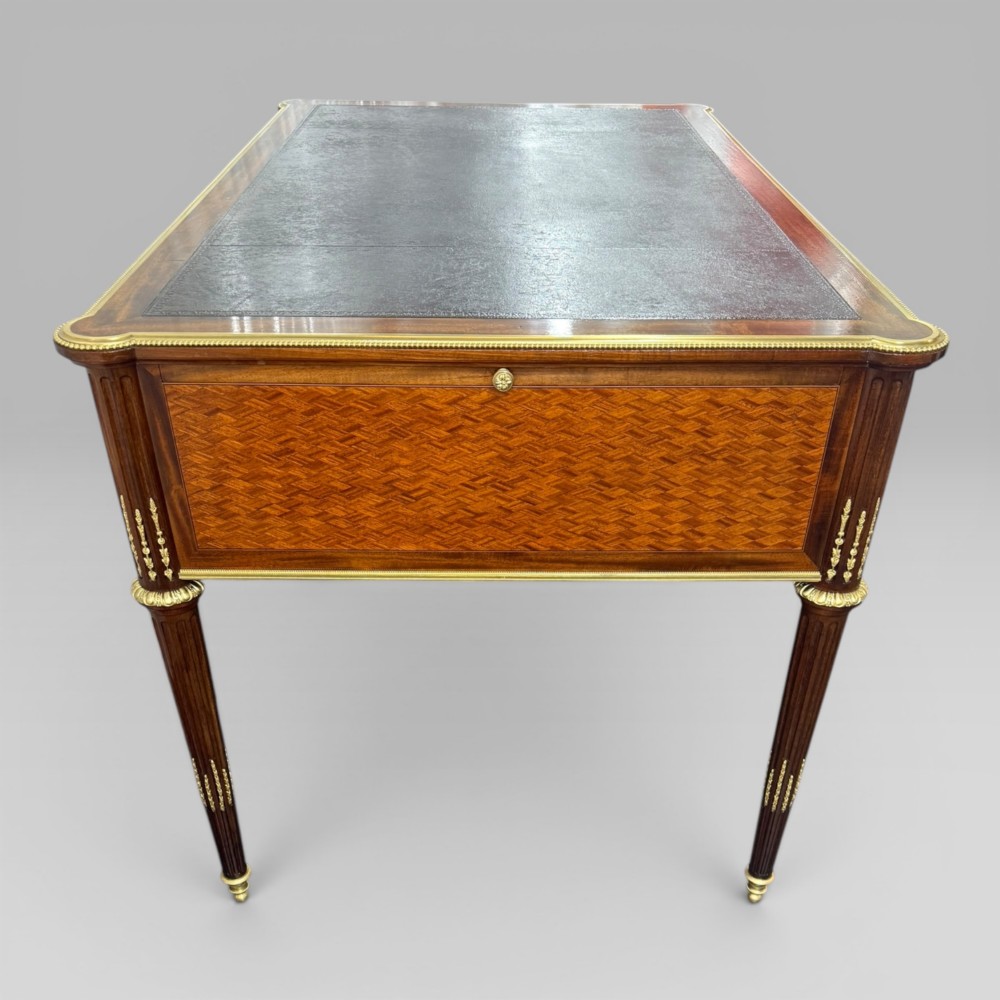 A Louis XVI style mahogany and parquetry writing desk featuring a dark leather top, gilt-bronze mounts, five drawers, and fluted tapered legs. View VIII