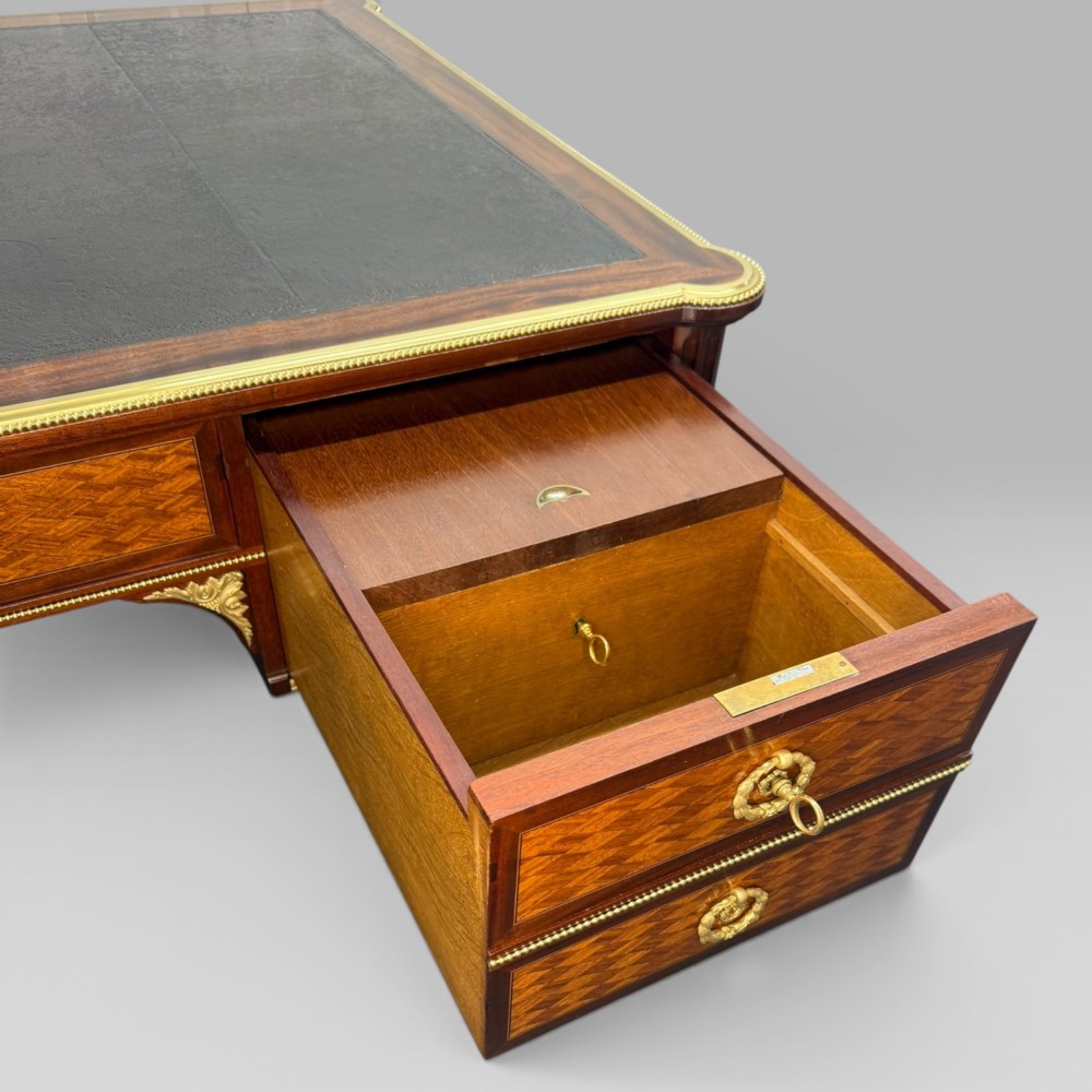 A Louis XVI style mahogany and parquetry writing desk featuring a dark leather top, gilt-bronze mounts, five drawers, and fluted tapered legs. View XII