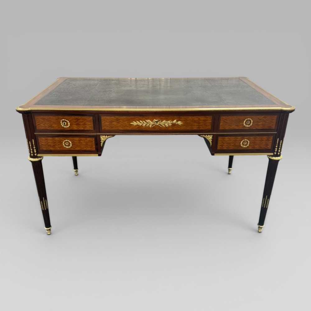 A Louis XVI style mahogany and parquetry writing desk featuring a dark leather top, gilt-bronze mounts, five drawers, and fluted tapered legs. View XIV
