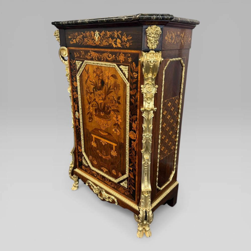 A nineteenth-century dark wood pier cabinet featuring detailed floral marquetry, polished gilt-bronze mounts, classical mask figures, and a black marble top.