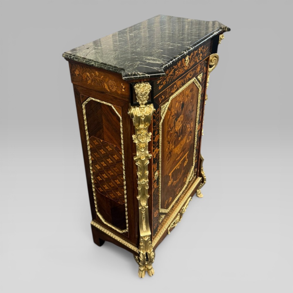 A nineteenth-century dark wood pier cabinet featuring detailed floral marquetry, polished gilt-bronze mounts, classical mask figures, and a black marble top. View V