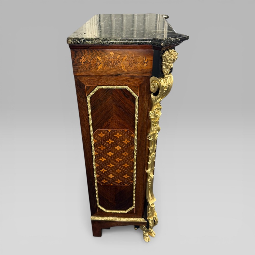A nineteenth-century dark wood pier cabinet featuring detailed floral marquetry, polished gilt-bronze mounts, classical mask figures, and a black marble top. View VI