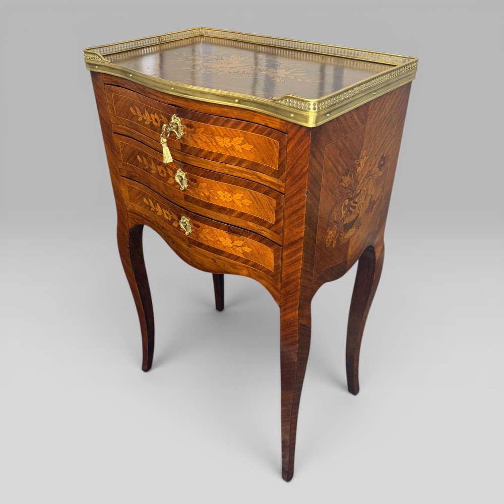A French Louis XV style kingwood petite commode featuring three floral marquetry drawers, cabriole legs, and a brass gallery top.