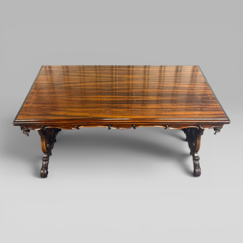 An Early Victorian rectangular centre table featuring a figured zebrawood veneered top, carved aprons, and carved rosewood trestle standards with scrolled feet. View II
