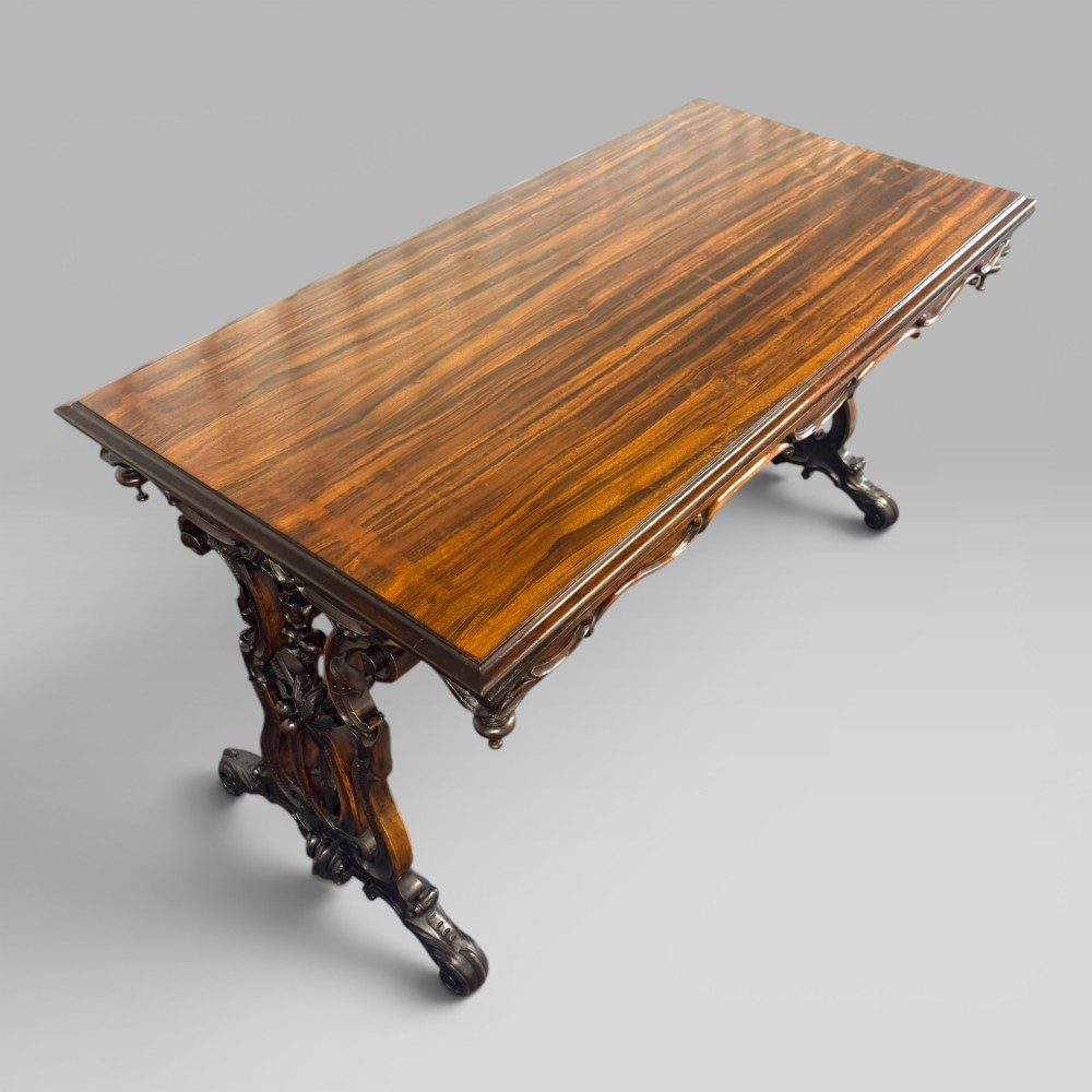 An Early Victorian rectangular centre table featuring a figured zebrawood veneered top, carved aprons, and carved rosewood trestle standards with scrolled feet. View III