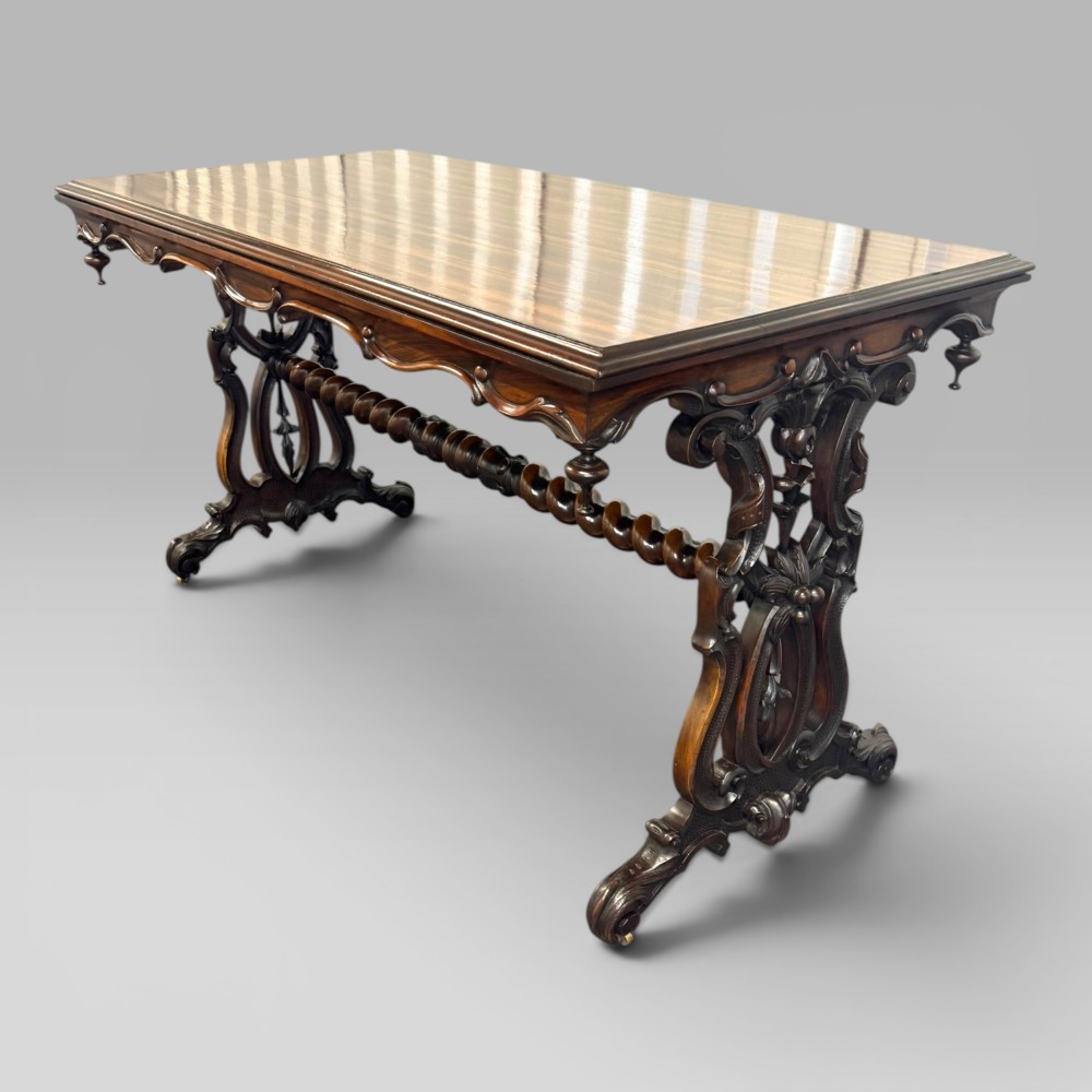 An Early Victorian rectangular centre table featuring a figured zebrawood veneered top, carved aprons, and carved rosewood trestle standards with scrolled feet. View IV